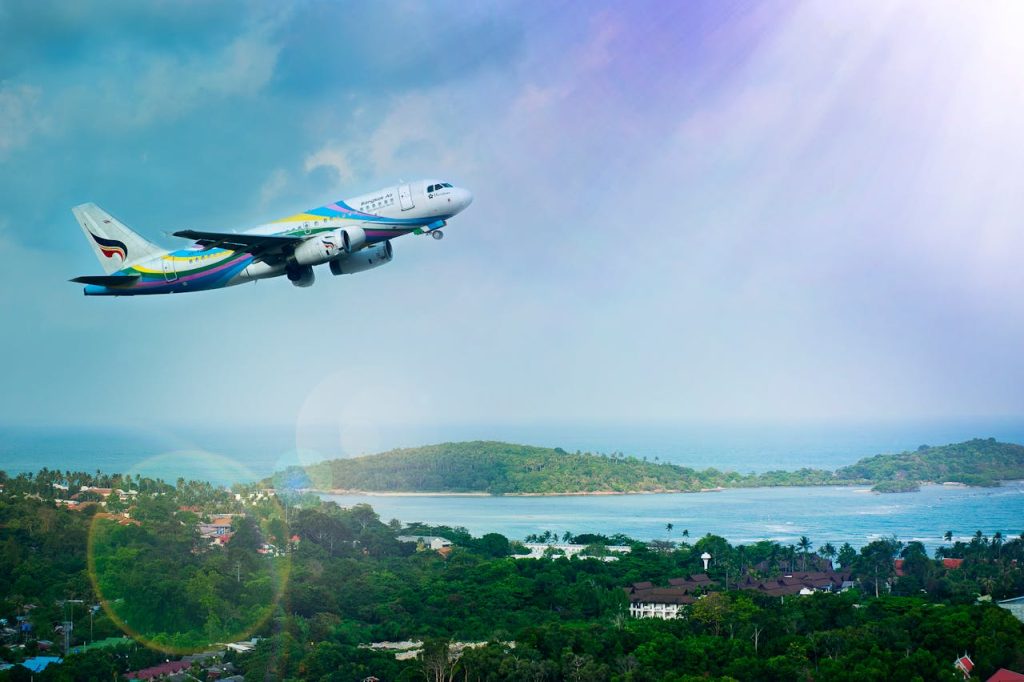 Airplane soaring over Koh Samui island, Thailand, showcasing a vibrant tropical landscape in daylight.